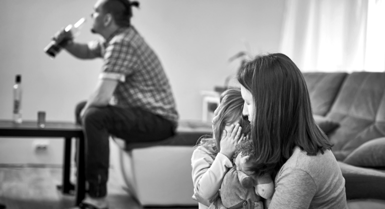 Man drinking alcohol and woman consoling child