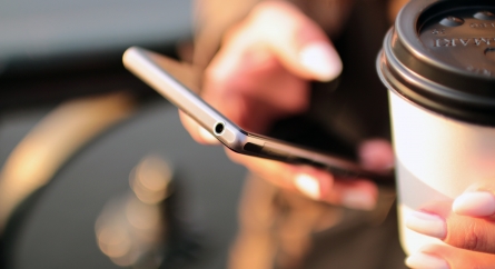 Hands holding a to-go coffee cup and a cell phone.