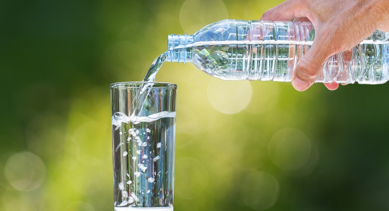 Hand holding a plastic bottle water and pouring water into a glass.