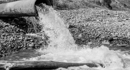 Water pouring out of a pipe into a smaller body of water surrounded by stones.