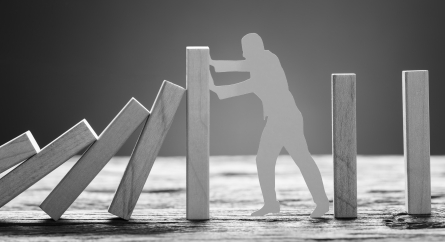 Paper man stopping wooden domino blocks on table against gray background.