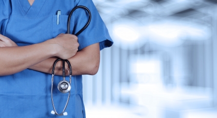 Doctor in scrubs holding a stethoscope with arms crossed.