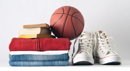 White converse high-tops next to a stack of clothes, books, and a basketball