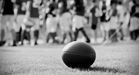 Close up of an American football on the field, players in the blurred background.