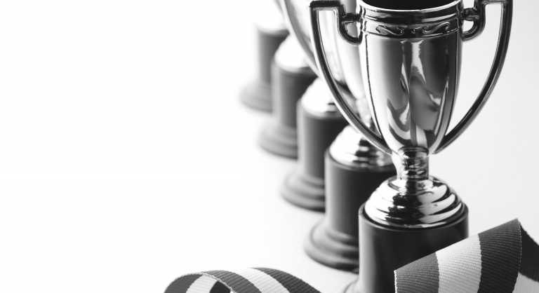 A row of trophies and a red, white, and blue ribbon.