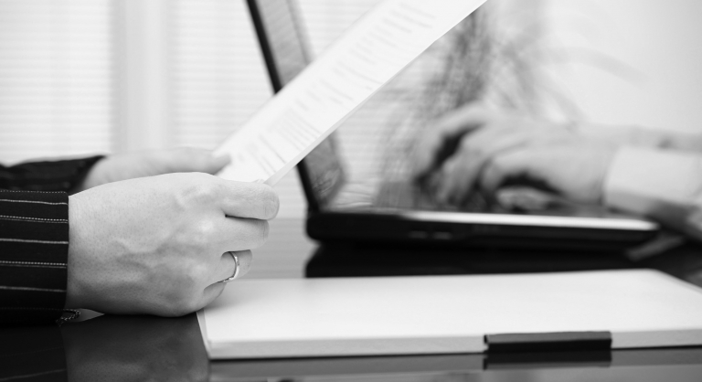 Lawyer is reading contract and business client is typing on laptop.