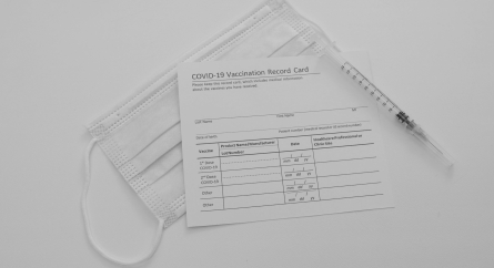 Medical mask and COVID-19 vaccine on vaccination record card.