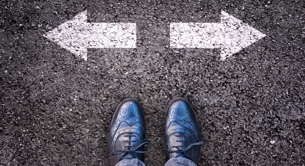 Two feet on a paved road in front of two arrows pointing in opposite directions.