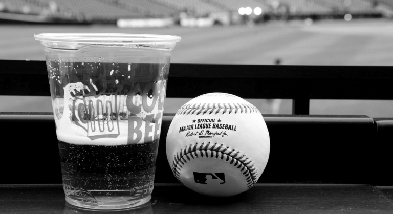 Beer in a plastic cup next to a baseball at a game.