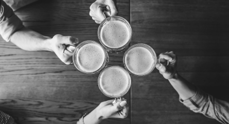 Top view of four people holding mugs with beer cheersing.