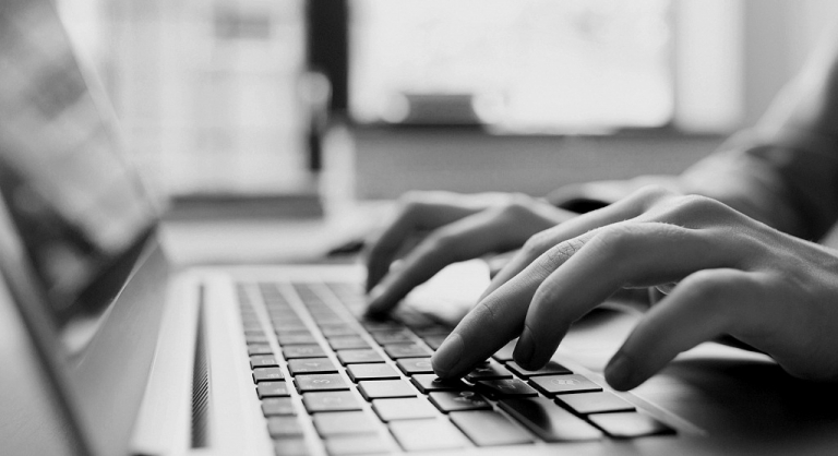 Close-up side-view of hands typing on a laptop.