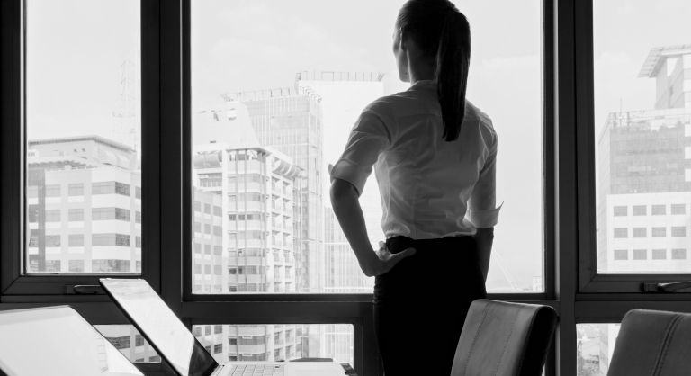 Businesswoman standing with her hand on her hip in an office looking out the window.