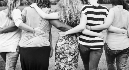 Group of women walking with their backs facing the camera and arms around each others shoulders and waists.