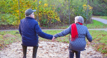 An elderly couple sitting on swings holding hands.