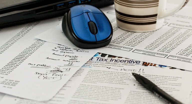 Tax documents with a laptop, mouse, pen, and mug.