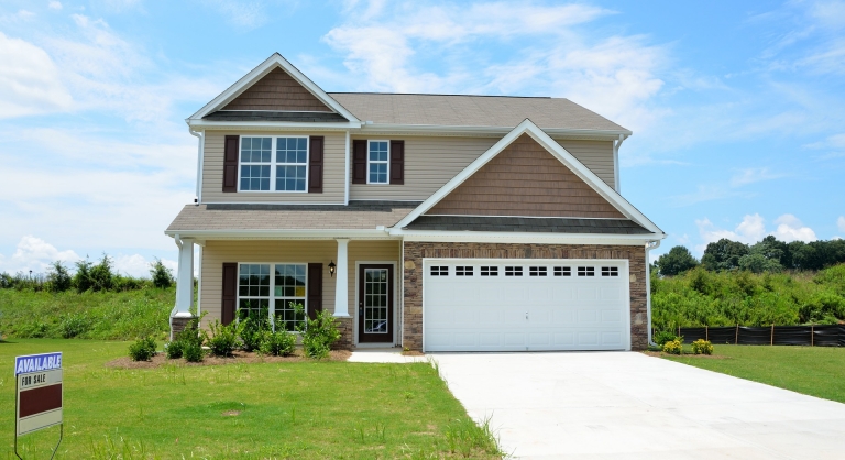 A suburban house on a large plot of land with a for sale sign.