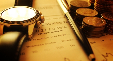 A watch, pen, and stacks of coins on a financial document.