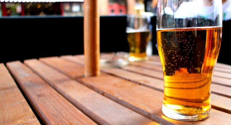 Two glasses of beer on a wooden outdoor umbrella table.
