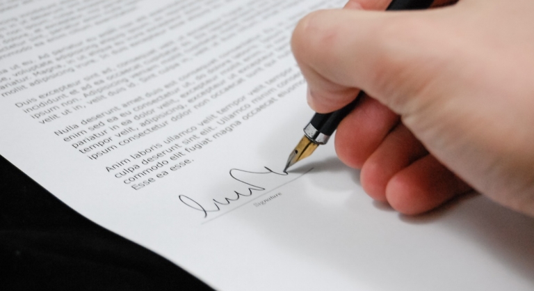 Person signing a document with a fountain pen.