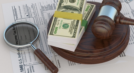 Magnifying glass, gavel, and stacks of money on an income tax return form.