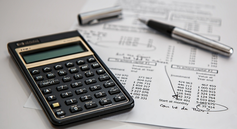 Calculator and pen on a paper where someone was calculating budget with the words "can we do this?" written on the bottom.