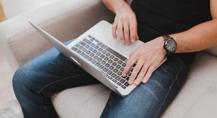 Person using a laptop on their lap while sitting on a couch.