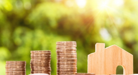 Stacks of coins next to a wooden house block.