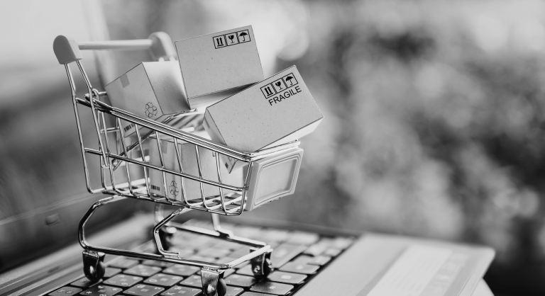 Mini shopping cart with four boxes labeled fragile inside it sitting on an open laptop.