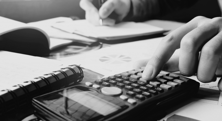 Close-up of a hand using a calculator and doing finance at home office while writing notes in a notebook.