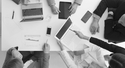 Top-down view of employees working together with laptops, smartphones, and charts.