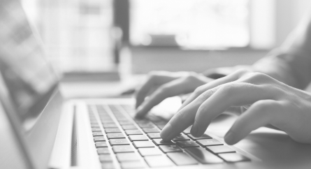 Close-up side-view of hands typing on a laptop.