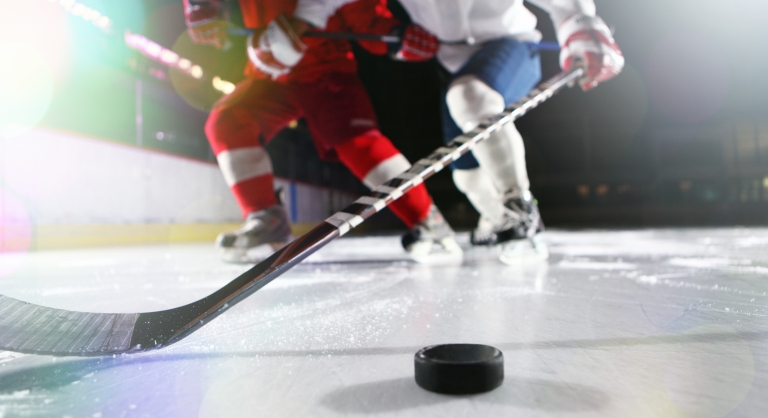 Ice-level image of male ice hockey players in a tackle during a game.