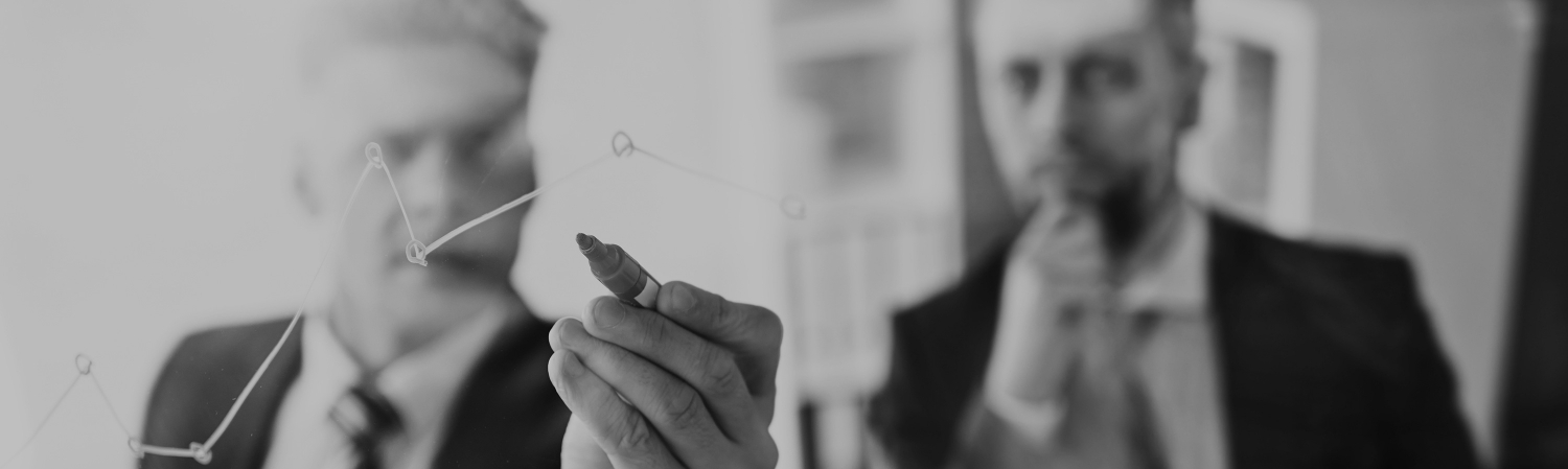 Two businessmen looking at a graph on a clear whiteboard.