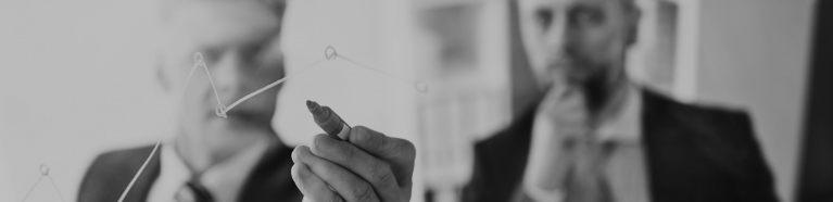 Two businessmen looking at a graph on a clear whiteboard.