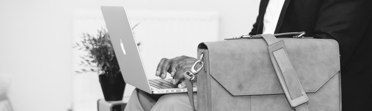 Someone typing on a laptop with a briefcase next to them.