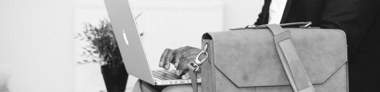 Someone typing on a laptop with a briefcase next to them.