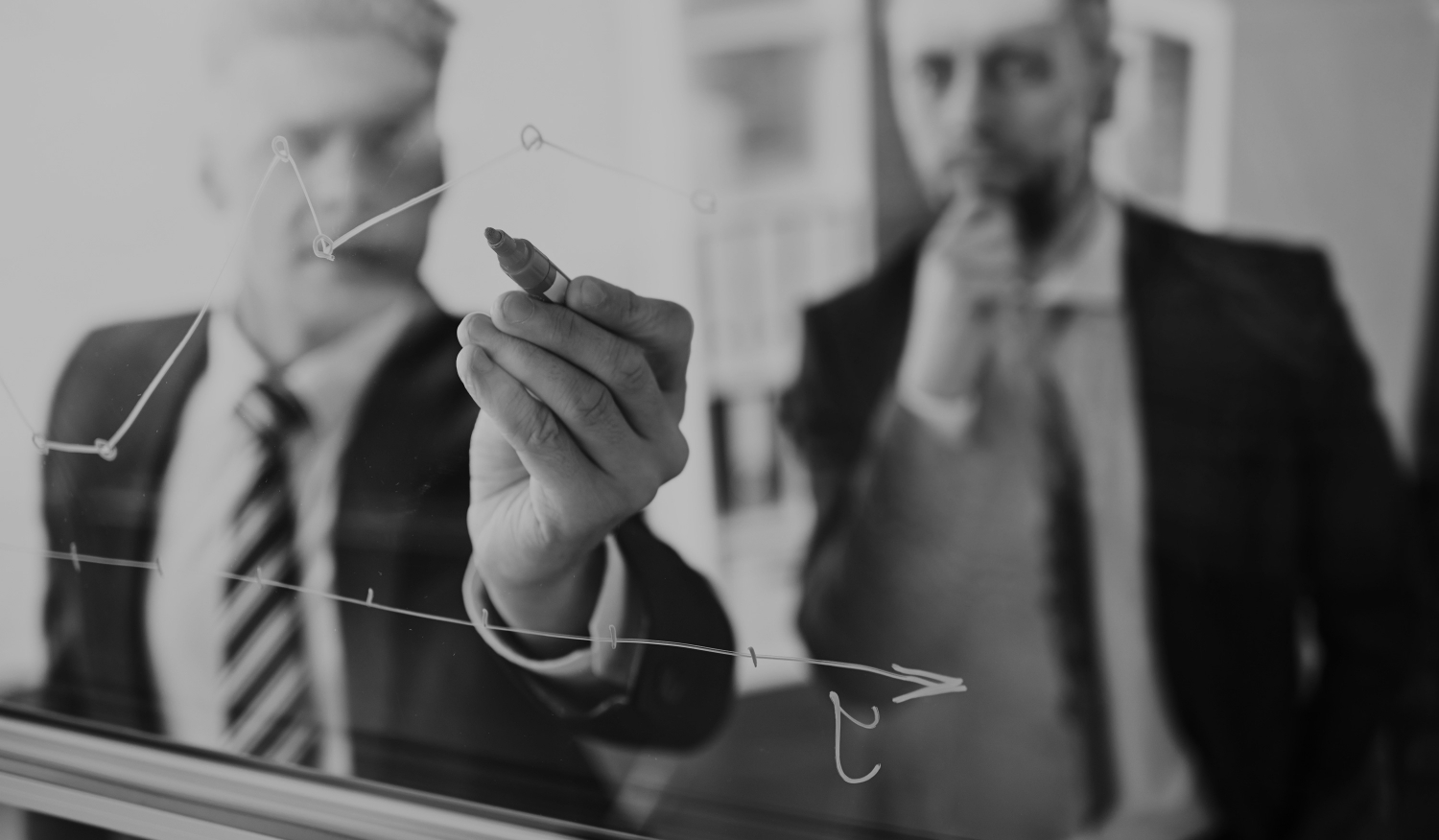 Two businessmen looking at a graph on a clear whiteboard.