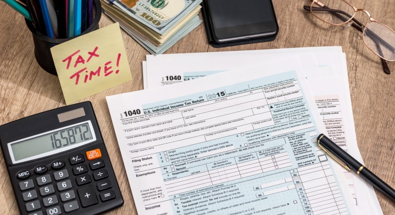 Tax form with calculator, money and pen on a table.