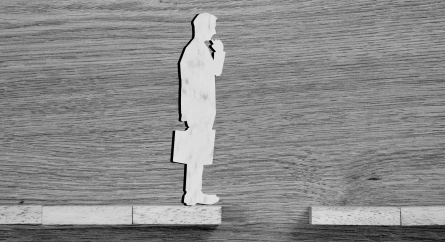 Wooden businessman silhouette contemplating over a gap in a wood block road.