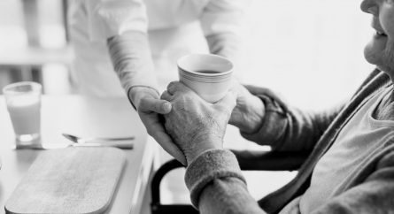 Elderly woman in an assisted living being handed a cup of coffee from a staff member.