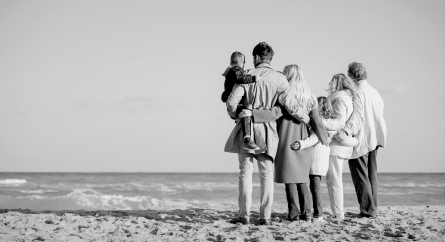 Shot from behind of a multigenerational family in coats on the beach.
