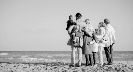Shot from behind of a multigenerational family in coats on the beach.
