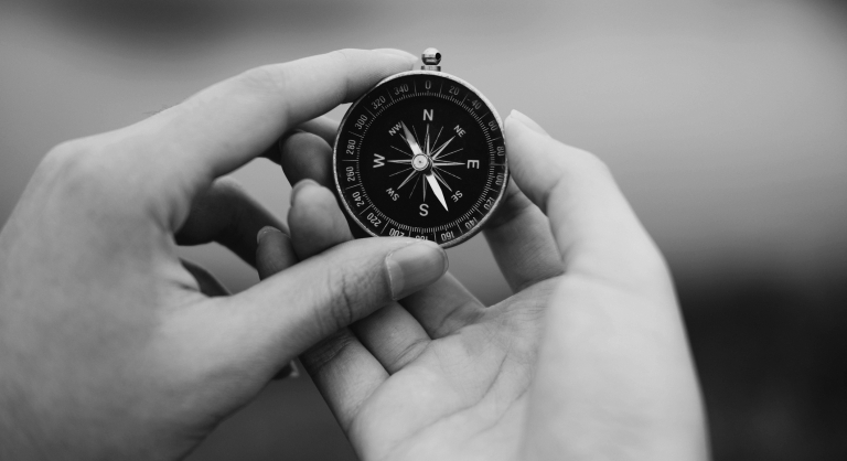 Hands holding compass for searching direction outdoor.