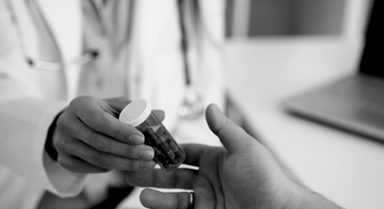 Pharmacist handing patient medicine in a clear pill bottle.