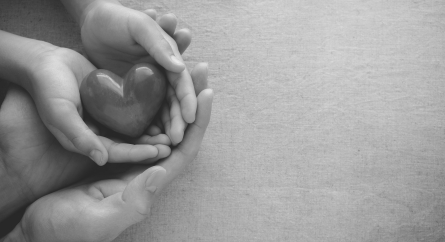 Adult and child hands holding a smooth stone heart.
