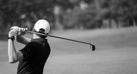 A man hits the perfect golf shot from the fairway towards the putting green.