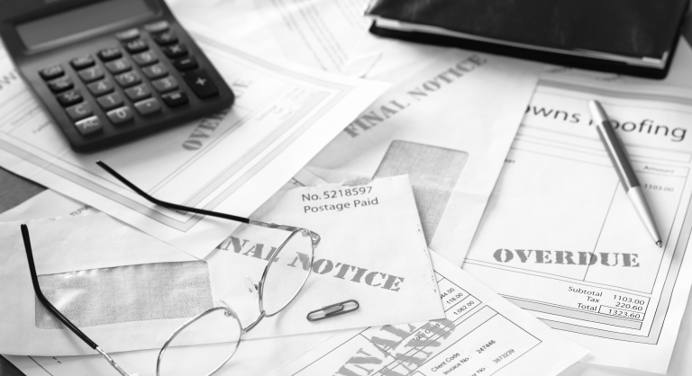 Unpaid bills on table with calculator, glasses, and a checkbook.