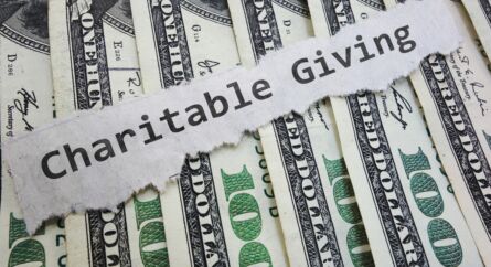 The words charitable giving on a note on top of $100 dollar bills