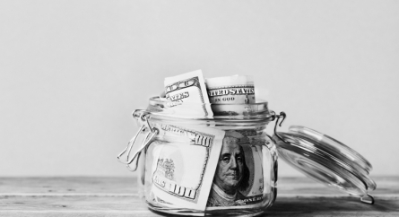 Dollar bills in glass jar on wooden table.