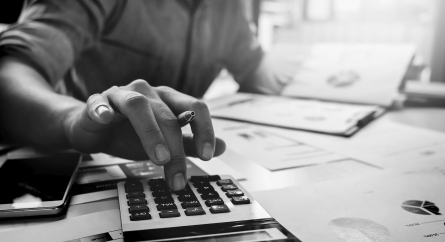 Person using a calculator with charts scattered across their desk.